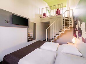 Une chambre d’hôtel avec un lit, un téléviseur fixé au mur, un escalier avec une rampe et un tableau accroché au mur.