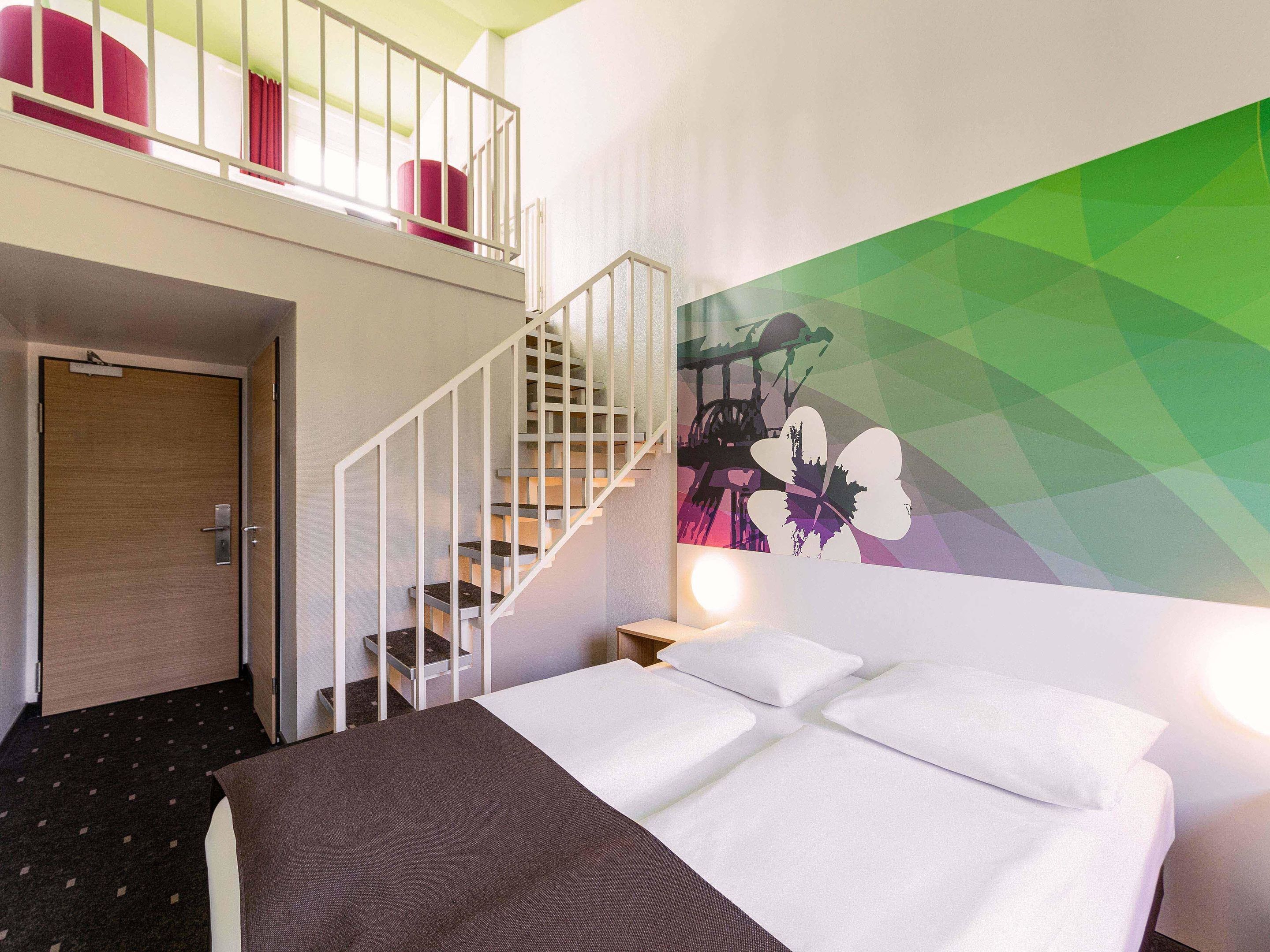 Ein Hotelzimmer mit Bett, einer Wendeltreppe, Wandgemälde und einem Balkon mit roten Kissen.