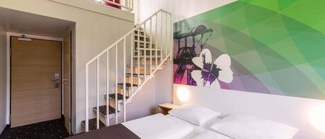 A hotel room with a bed, a staircase, a wall mural, and a balcony with red cushions.