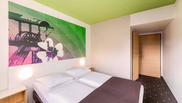 Ein Hotelzimmer mit einem Bett, einem Kunstwerk an der Wand, einem Nachttisch und einer Tür zu einem anderen Raum.