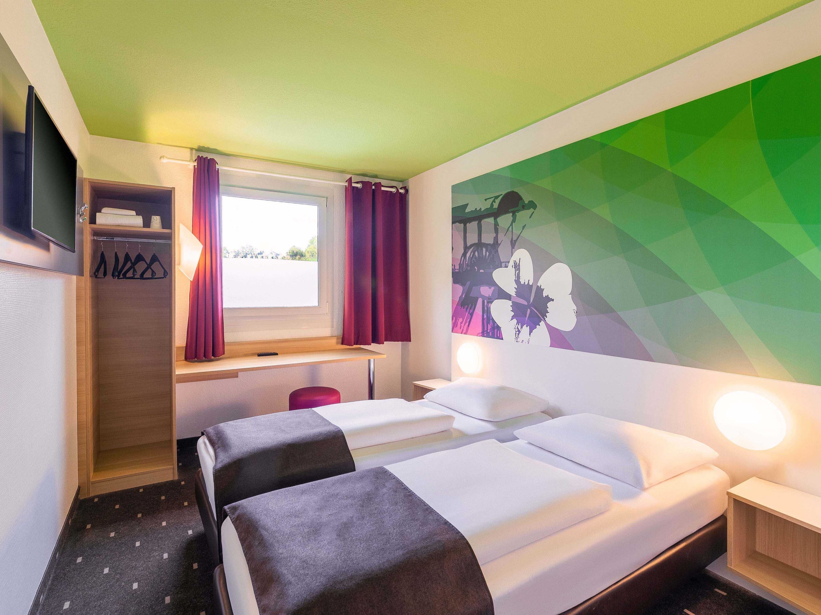 Habitación de hotel con cama, escritorio, armario y un cuadro de flores geométricas en la pared.