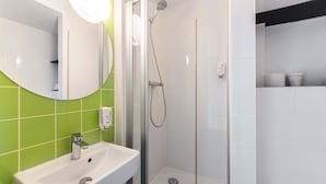 Une salle de bain avec une douche à parois de verre, un lavabo blanc et un mur recouvert de carreaux verts.