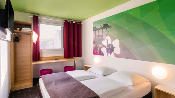 Une chambre d’hôtel équipée d’un lit, d’un bureau, d’une chaise, d’une armoire et d’une fenêtre avec des rideaux.