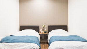 A hotel room with two beds, a nightstand, and a wall-mounted light. - Mita Guest House (Tokyo)