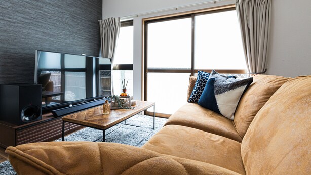 A modern living room with a large flat-screen TV, a wooden coffee table, and a beige sofa with patterned cushions. - Mita Guest House (Tokyo)