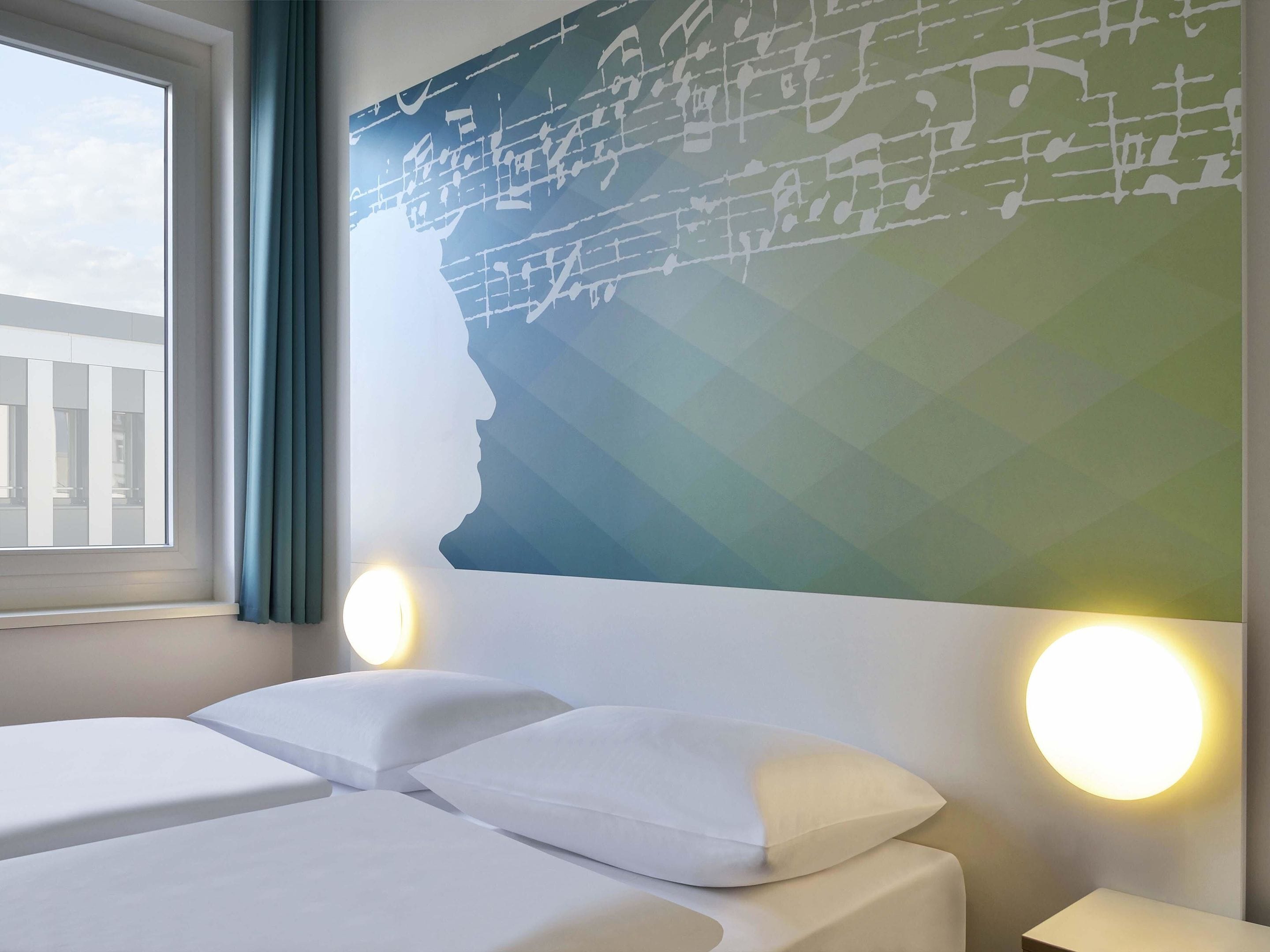 Een hotelkamer met een bed, twee nachtkastjes, een raam en een muur met een geometrisch patroon.
