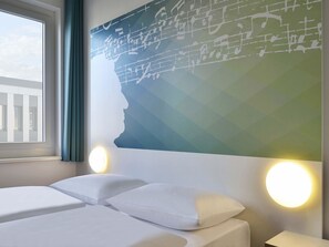 Habitación de hotel con una cama, dos mesitas de noche, un ventanal y una pared con diseño geométrico.