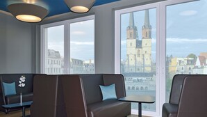 A modern lounge area with leather seating, a small table, and large windows offering a view of a historic building. - B&B HOTEL Halle (Saale) (Halle (Saale))