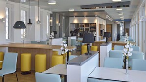 A modern hotel lobby with a central bar area, seating arrangements, and a reception desk. - B&B HOTEL Halle (Saale) (Halle (Saale))