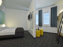 Una habitación de hotel moderna con una cama litera, un escritorio, dos otomanas amarillas y un televisor montado en la pared.