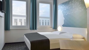 A hotel room with a bed, a desk, and two windows with curtains. - B&B HOTEL Halle (Saale) (Halle (Saale))