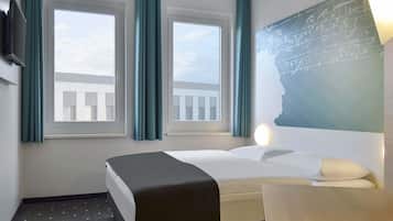 A hotel room with a bed, a desk, and two windows with curtains.