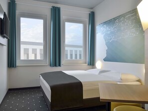 Habitación de hotel con una cama, un escritorio y dos ventanas con cortinas.