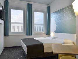 Habitación de hotel con una cama, un escritorio y dos ventanas con cortinas.