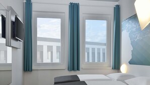 A hotel room with a bed, a desk, a chair, a TV, and windows with curtains. - B&B HOTEL Halle (Saale) (Halle (Saale))
