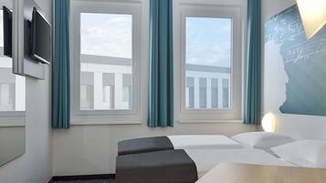 A hotel room with a bed, a desk, a chair, a TV, and windows with curtains.