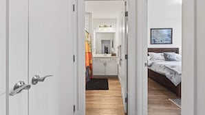 A narrow hallway leading to a bedroom with a bed, a bedside table, and a nightstand.