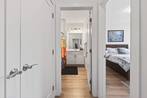 A narrow hallway leading to a bedroom with a bed, a nightstand, and a mirror.