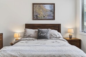 Une chambre à coucher avec un lit, deux lampes de chevet, un tableau encadré au mur et une fenêtre avec des stores.