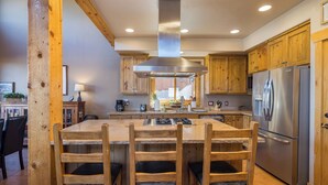 A kitchen with wooden cabinets, a stainless steel refrigerator, and a central island with chairs. - Coyote Run - Cozy Rustic Retreat in Moab- Private Hot Tub-Fireplace (moab)
