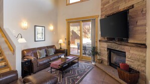 A living room with a leather sofa, a coffee table, a fireplace, a TV, and a staircase. - Coyote Run - Cozy Rustic Retreat in Moab- Private Hot Tub-Fireplace (moab)