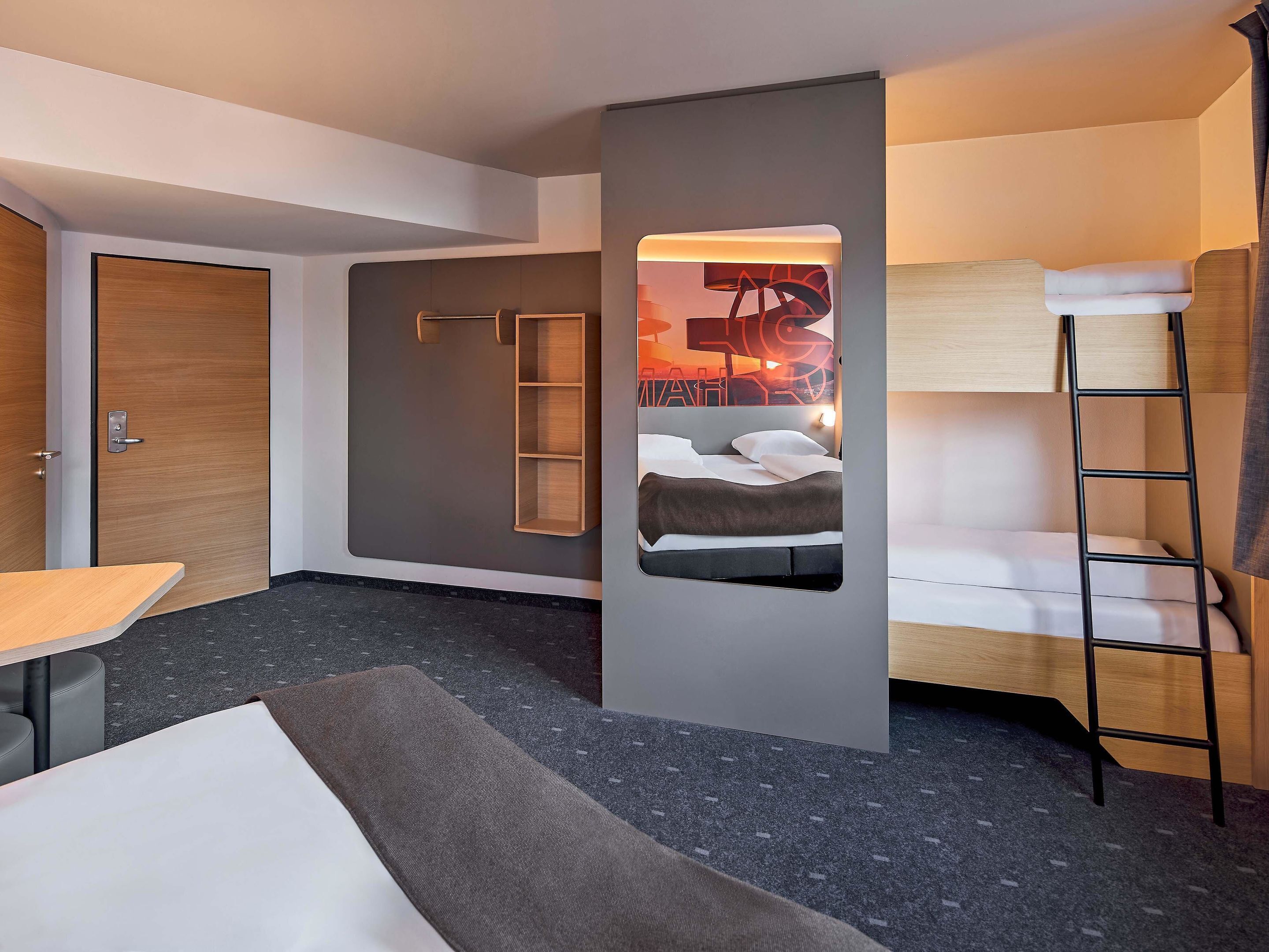 A modern hotel room with a bunk bed, a desk, and a wardrobe.