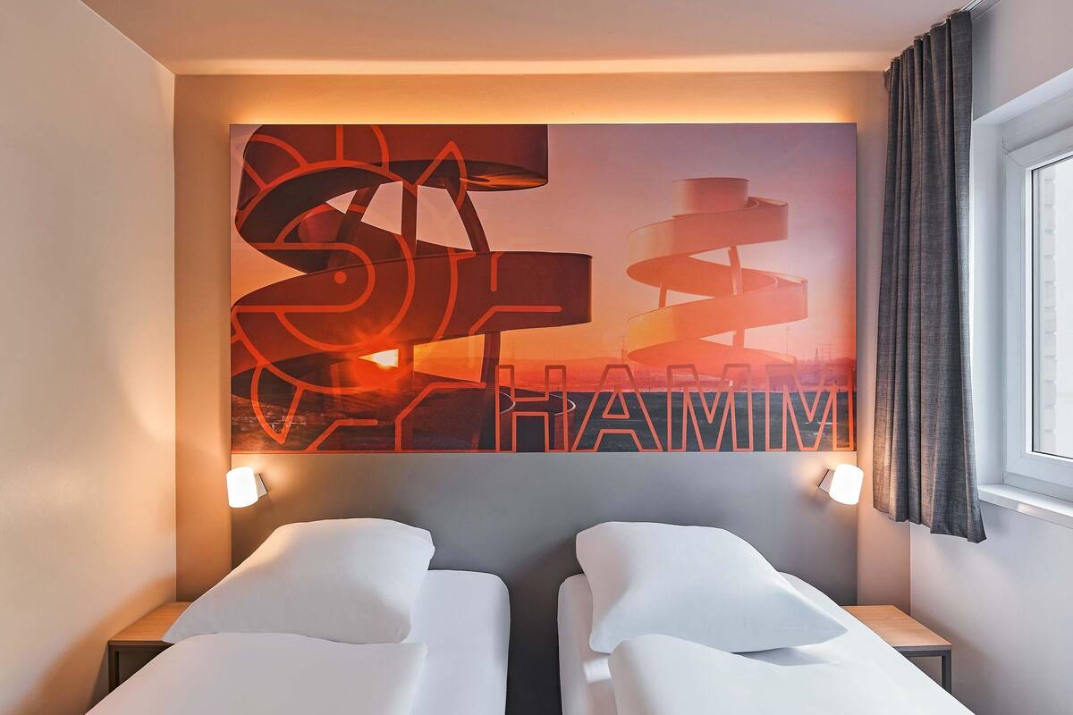 A hotel room with two beds, a wall art piece, and a window with curtains.