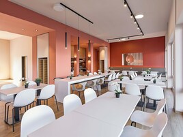 A modern dining area with white tables and chairs, pendant lighting, and a red accent wall.
