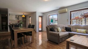 A modern living room with a sofa, coffee table, and dining area. There is a large window with a view of the outside. - Holiday home with balcony for 6 people (Bribir)