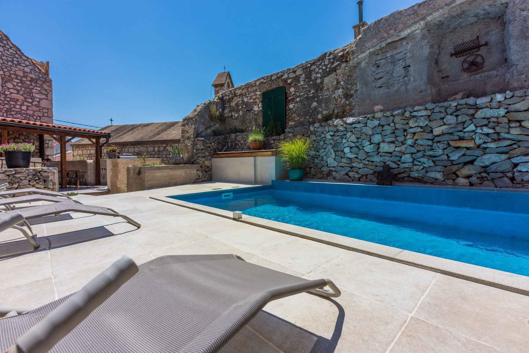 A stone-walled pool area with lounge chairs and potted plants.