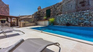 A stone-walled pool area with lounge chairs and potted plants. - Holiday home with balcony for 6 people (Bribir)