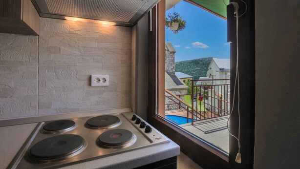 A kitchen with a built-in stove, a window with a view of a balcony, and a stone-textured wall. - Holiday home with balcony for 6 people (Bribir)