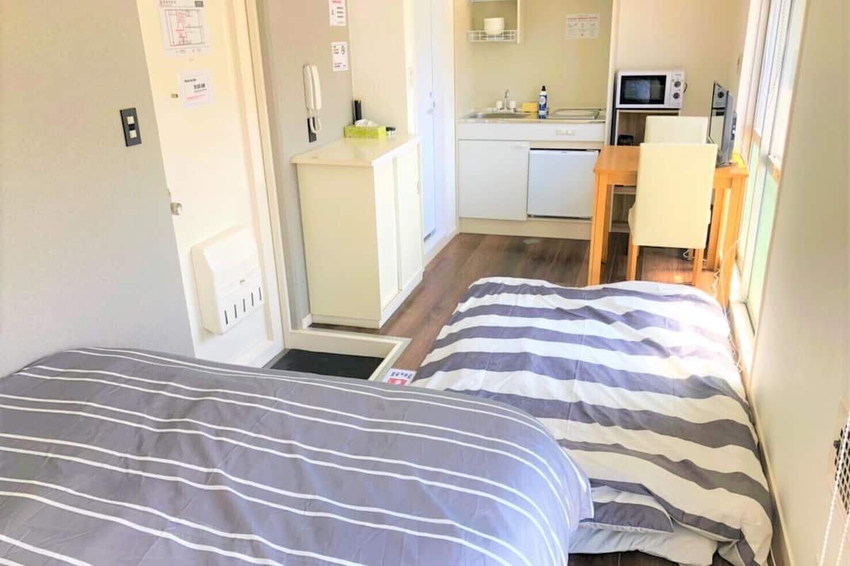 Une chambre de taille modeste comprenant deux lits, un coin cuisine et une petite salle de bain.
