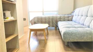 Una habitación con un sofá, una mesita, un estante con objetos y una ventana.