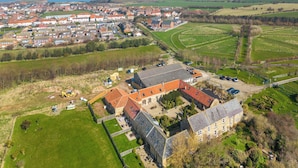 An aerial view of a large estate with multiple buildings, including a main house with a red-tiled roof, surrounded by well-maintained gardens and fields. - Seaton Court - UK31955 (Staithes)