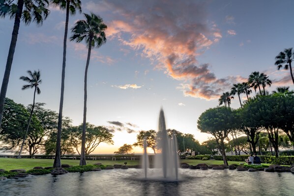A fountain in a park with palm trees and a sunset in the background. - Kamaole Sands Remodeled 1 Bed 2 bathroom, Split AC, king bed (Kihei)