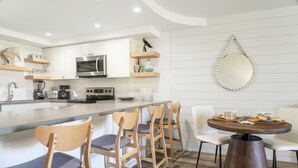 Een moderne keuken met witte kasten, een centraal eiland met barkrukken en een eethoek met een ronde tafel.