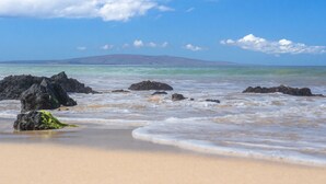 Een strand met heldere lucht, kalm water en rotsachtige rotsformaties.