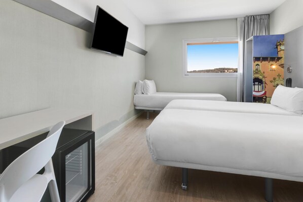 A hotel room with two beds, a TV, a desk, and a window with a view.