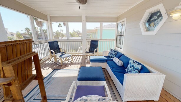 A covered porch with a white wicker sofa, blue cushions, and a wooden chair. - Private Heated Pool, Golf Cart Included and Close To Beach (Port Aransas)