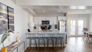 A modern kitchen with white cabinets, a central island with bar stools, a microwave, a stove, and a refrigerator. - Private Heated Pool, Golf Cart Included and Close To Beach (Port Aransas)