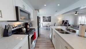 A modern kitchen with a built-in oven, microwave, and coffee maker. There is a dining area with a table and chairs, and a large window providing natural light. - Private Heated Pool, Golf Cart Included and Close To Beach (Port Aransas)