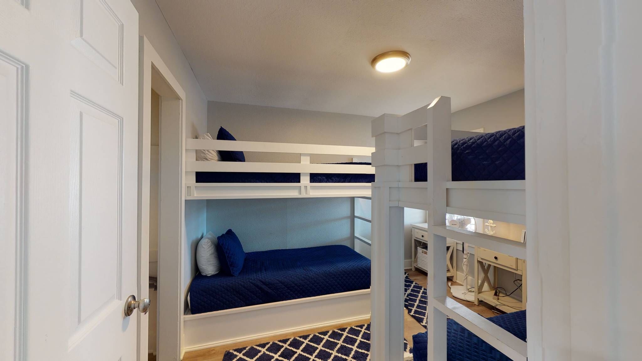 Une chambre avec un lit superposé, une porte blanche et un luminaire au plafond.