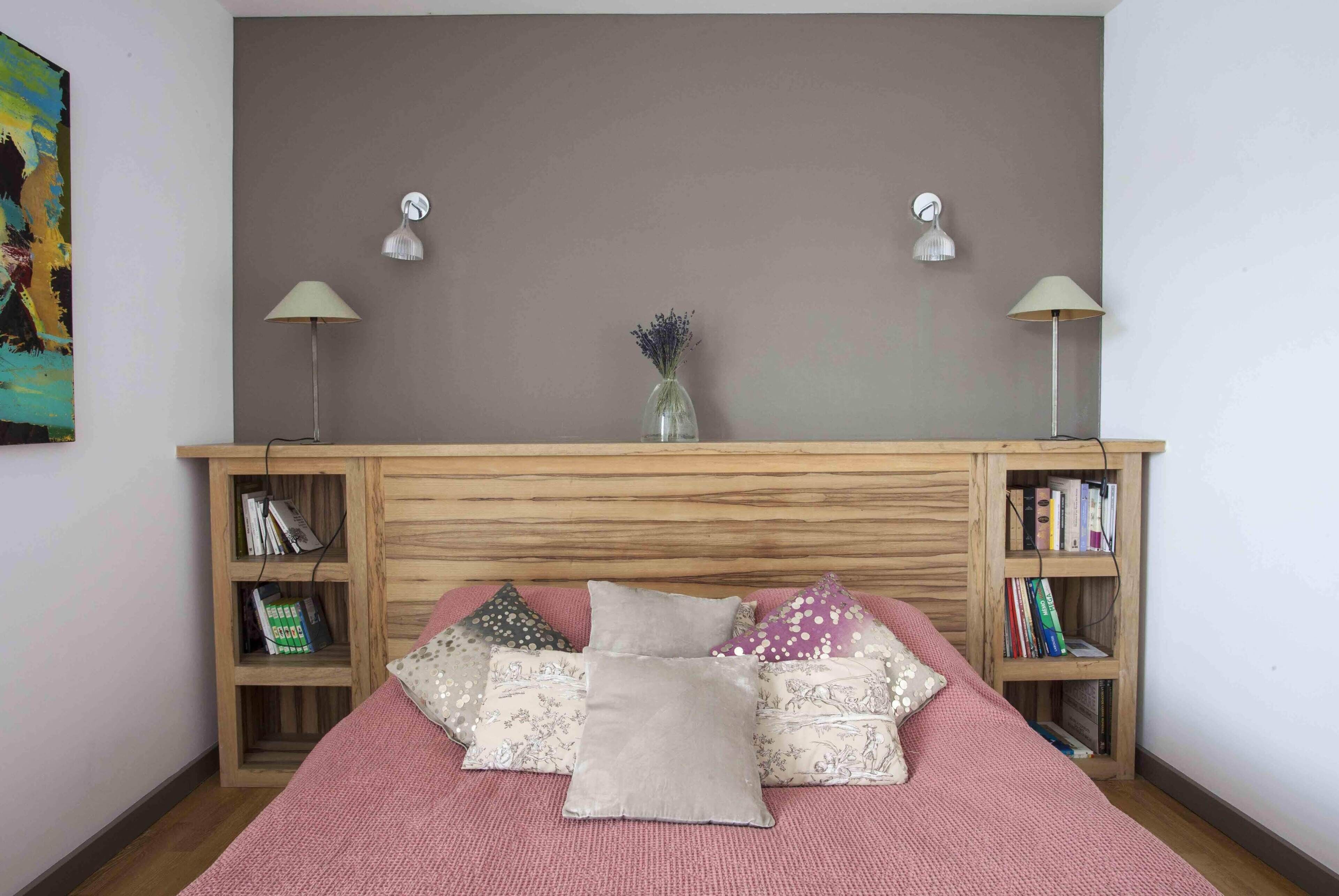 A bedroom with a wooden headboard, a pink bedspread, and multiple pillows. There are two bedside tables with lamps and bookshelves.