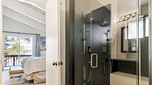 A modern bathroom with a glass shower enclosure, a vanity with a mirror, and a bed in the adjacent room. - Tahoe's Most Sought After Lakeview -Cliff Hanger Home less than 1 Mile to Heavenly, Sleeps 10 (South Lake Tahoe)