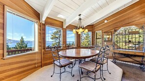 A wooden-paneled room with a round table and chairs, large windows with a view of trees and mountains, and a chandelier. - Tahoe's Most Sought After Lakeview -Cliff Hanger Home less than 1 Mile to Heavenly, Sleeps 10 (South Lake Tahoe)