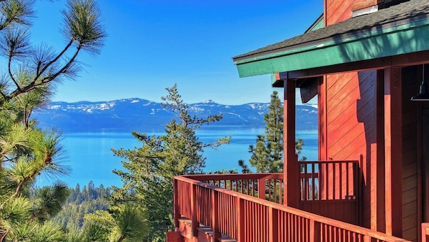 A red wooden cabin with a balcony overlooking a clear blue lake and mountains. - Tahoe's Most Sought After Lakeview -Cliff Hanger Home less than 1 Mile to Heavenly, Sleeps 10 (South Lake Tahoe)