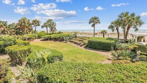 Um jardim ajardinado com palmeiras, um caminho e vista para a praia.