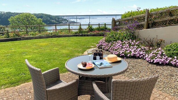 Une terrasse avec des meubles en osier, une table sur laquelle se trouve un livre, des verres à vin et un chapeau.
