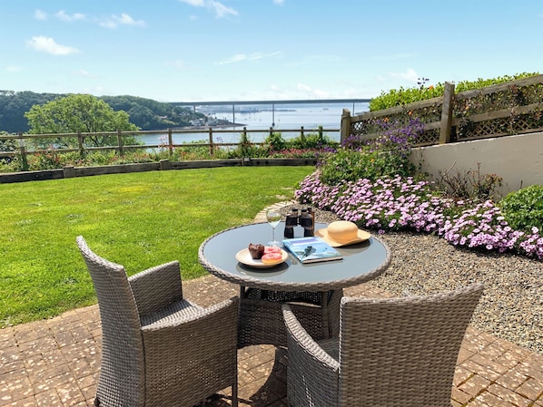 A patio with wicker furniture, a table with a book, wine glasses, and a hat.